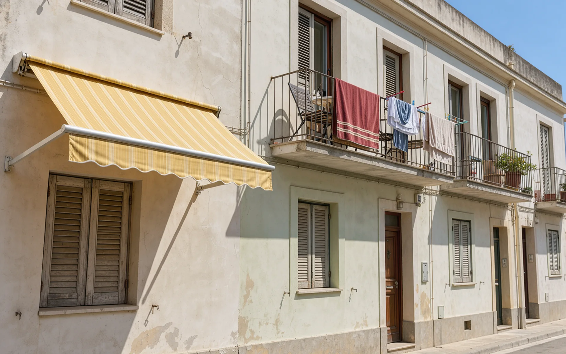 A yellow fabric awning shades a window beneath apartment balconies hung with laundry